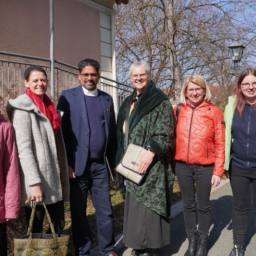 Eine Gruppe von Menschen steht vor einem Gebäude und lächelt für ein Foto. Sie sind alle für kaltes Wetter gekleidet. Der Mann in der Mitte trägt eine Brille und eine Krawatte.