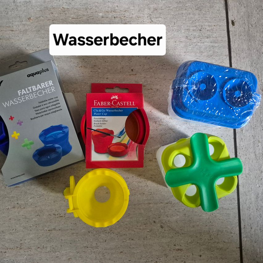 Ein Satz Wasserbecher, einige gefaltet und einige in ihrer Originalverpackung, liegen auf einer Betonoberfläche. Ein Becher ist blau und ein anderer gelb.
