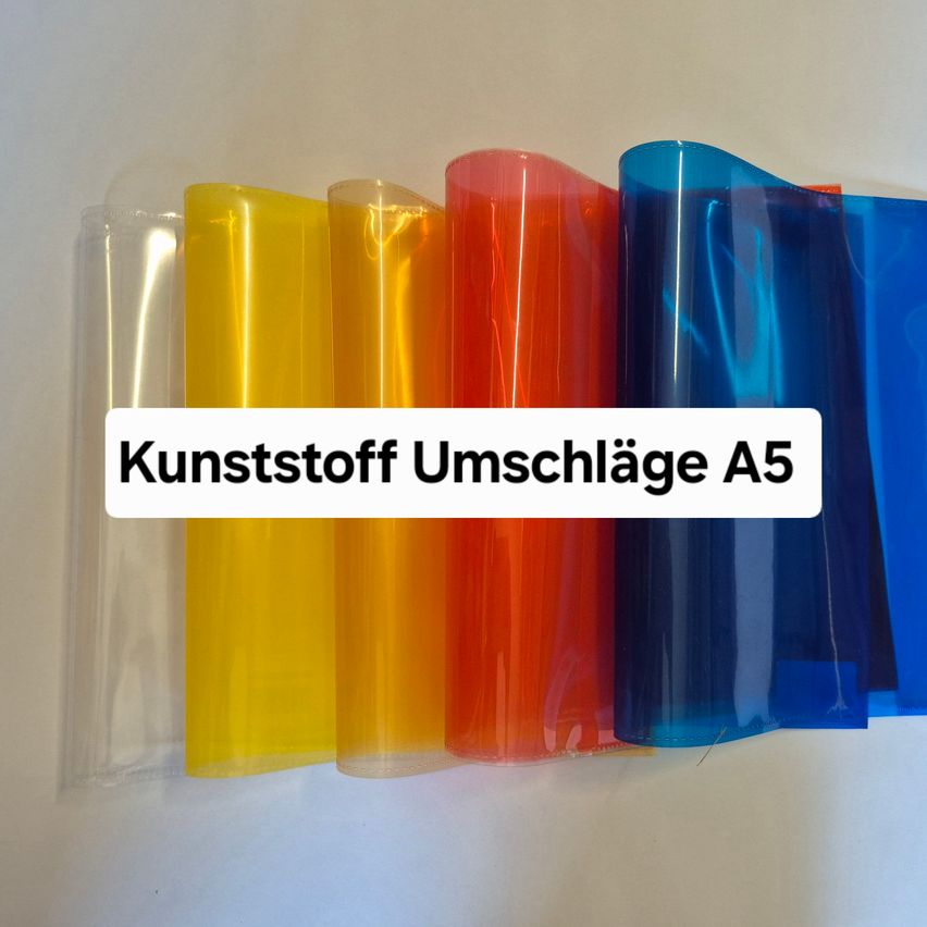 Fünf transparente Kunststofffolien in verschiedenen Farben, gelb, orange, rot und blau, sind auf einer weißen Oberfläche ausgelegt. Die Folien sind mit 'Kunststoff Umschläge A5' beschriftet.