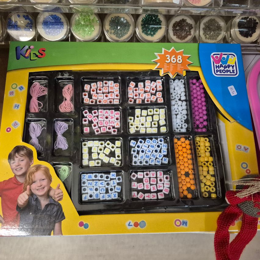 Eine bunte Bastelbox mit verschiedenen Perlen und Schnüren, gekennzeichnet mit '368', für Kinder. Sie enthält Alphabet- und Zahlenperlen. Ein Bild von zwei Kindern ist auf der Box.