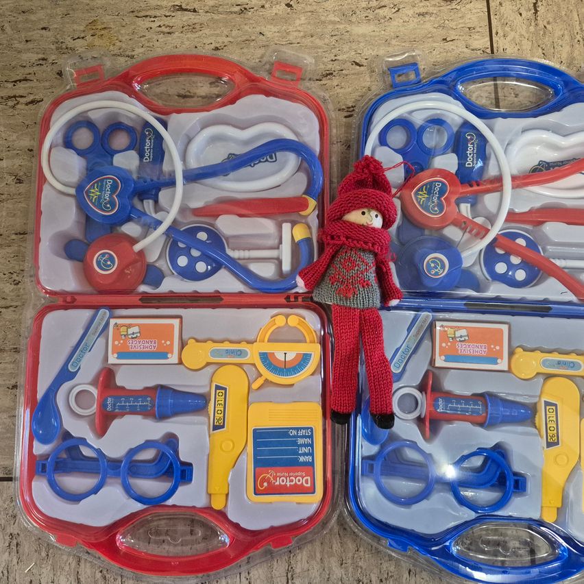 Zwei Arztkoffer sind auf einer Holzoberfläche ausgestellt. Jeder Koffer enthält verschiedene medizinische Instrumente, darunter Scheren, ein Thermometer und ein Stethoskop. Eine kleine Puppe steht zwischen den Koffern.