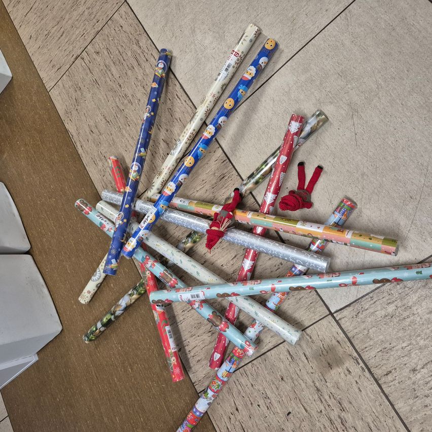 Ein Haufen Geschenkpapier auf einem Holzboden, einschließlich weihnachtlicher Designs, in unordentlicher Weise angeordnet.