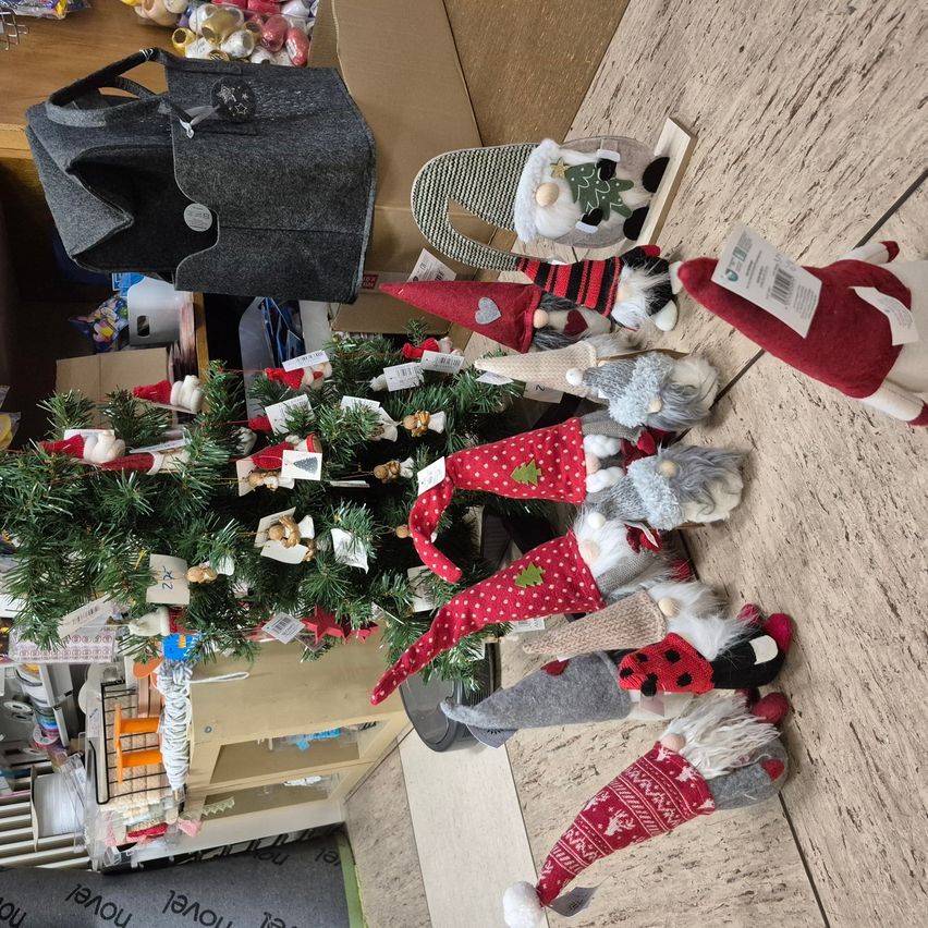 Ein Weihnachtsbaum ist von verschiedenen Gnomdekorationen mit roten und weißen Mützen umgeben, und eine graue Tasche liegt auf einer Holzoberfläche.