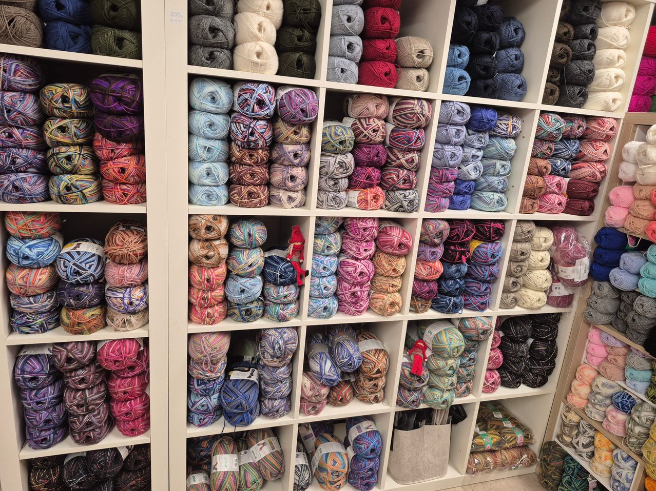 Ein Garnladen mit Regalen voller verschiedener Garne in verschiedenen Farben und Arten. Eine rote Puppe sitzt auf einem Regal.