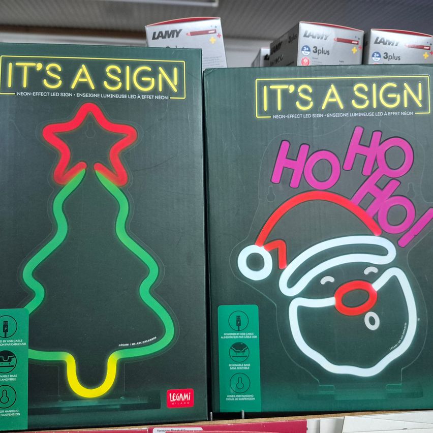 Zwei Neonschild-Boxen sind ausgestellt, eine mit einem leuchtenden Weihnachtsbaumdesign und die andere mit dem gezeichneten Santa Claus und den Worten 'Ho Ho Ho!' in Pink.