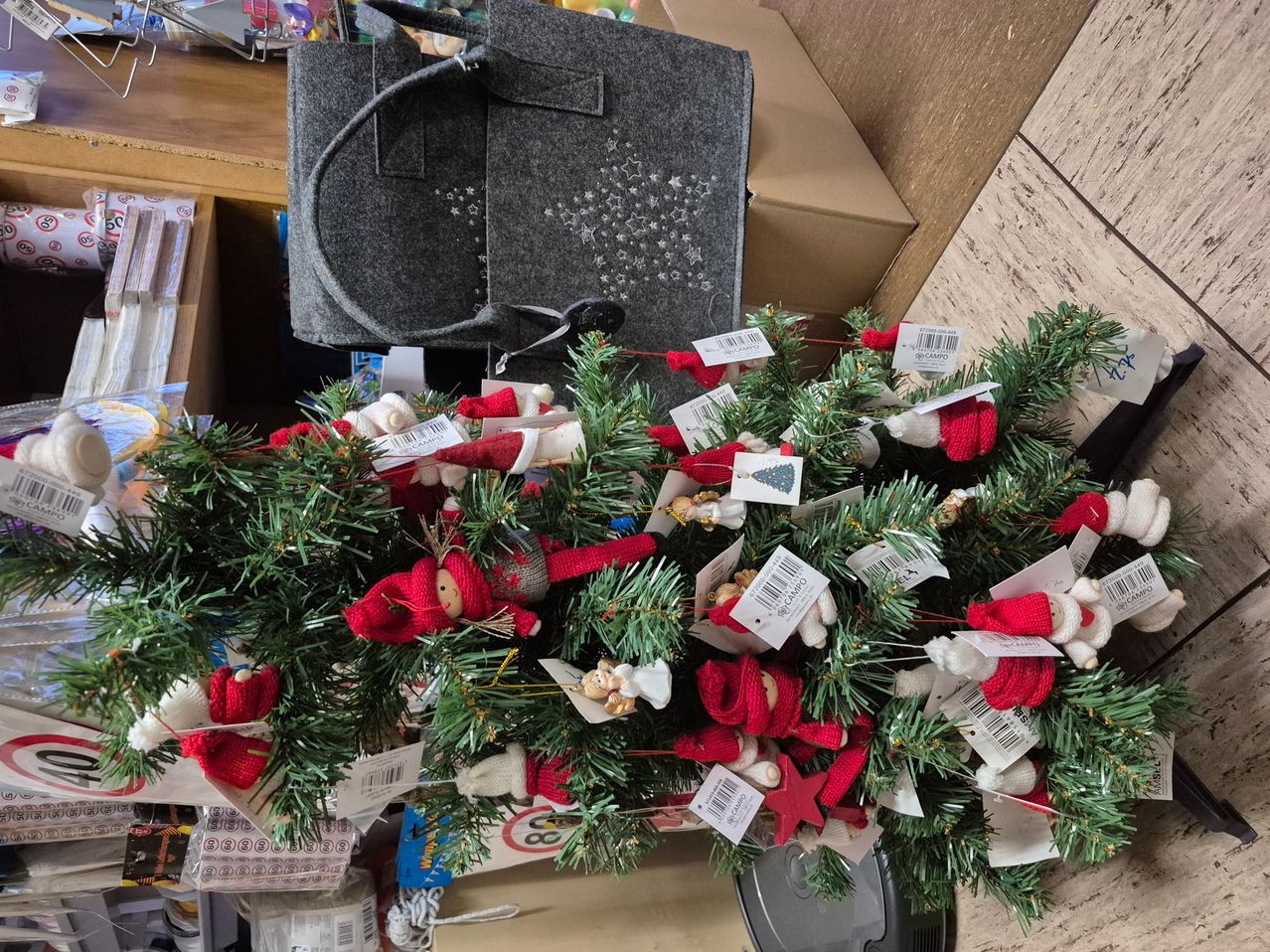 Ein mit Ornamenten, Etiketten und roten Schleifen geschmückter Weihnachtsbaum, der in einem Geschäft platziert ist, mit verschiedenen Artikeln im Hintergrund.