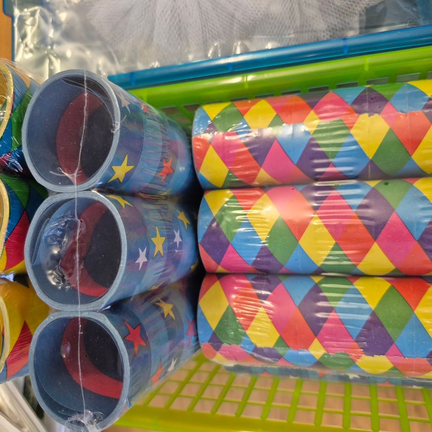 Ein Plastikkorb zeigt mehrere bunte Becher mit verschiedenen Mustern, einschließlich Sternen und einem Harlekin-Diamant-Design. Die Becher sind einzeln in Plastik verpackt.