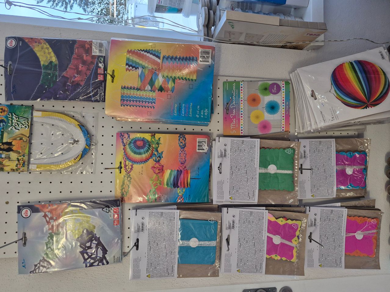 Eine Sammlung bunter Papierdekorationen und Partyzubehör ist an einer Wand ausgestellt, darunter Laternen, Banner und andere festliche Artikel.