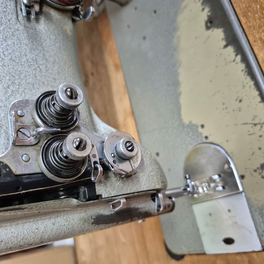 Ein Nahaufnahme einer alten Nähmaschine, die detaillierte Metallteile und einen hölzernen Hintergrund zeigt.