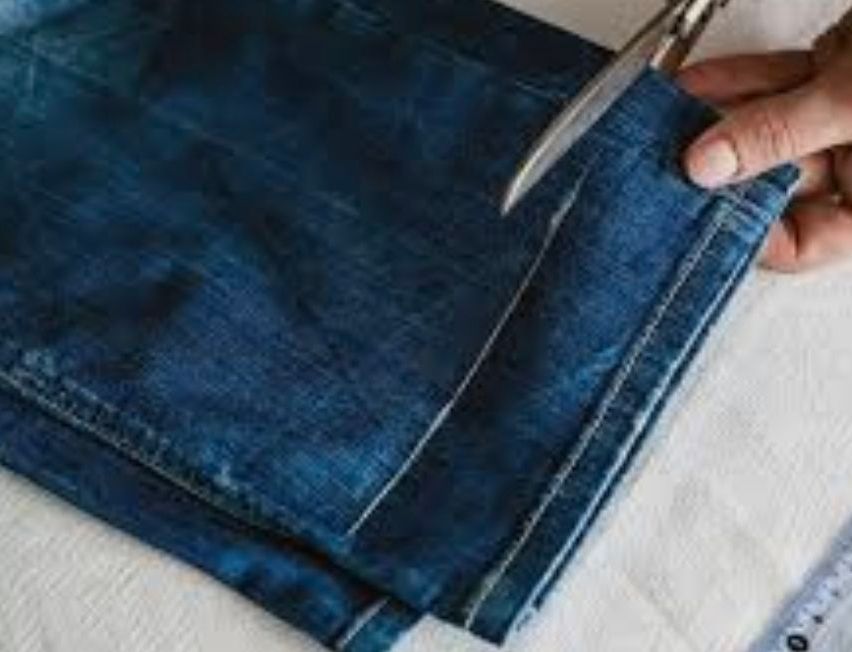Ein Paar blaue Jeans wird mit einer Schere geschnitten. Der Denim-Stoff ist gefaltet und der Schnitt wird entlang der Naht gemacht.