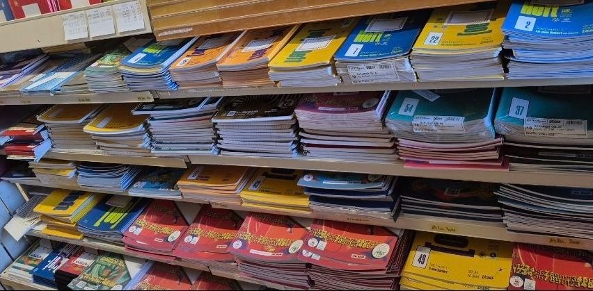 Ein Regal gefüllt mit ordentlich angeordneten Büchern in verschiedenen Farben und Größen, jedes mit einer Nummernbeschriftung. Die Bücher sind in Reihen gestapelt, wobei einige sichtbare Etiketten mit Zahlen und Text zeigen.