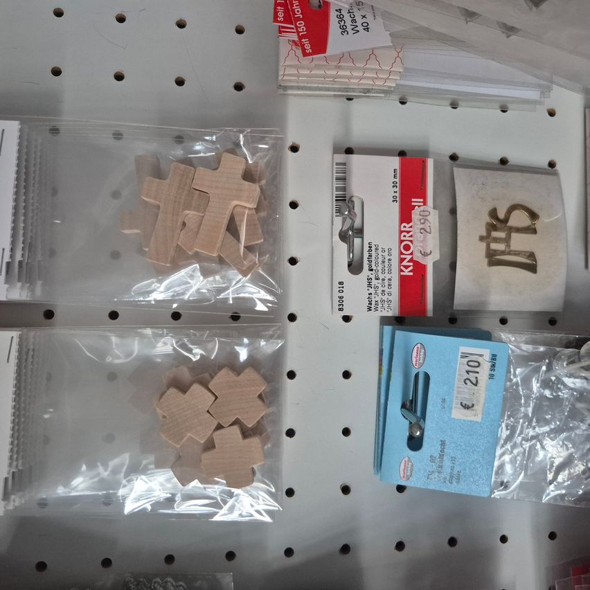 Verschiedene Holzpuzzleteile in durchsichtigen Plastiktüten, zusammen mit einer rot-weißen Schachtel mit der Aufschrift 'Knorr' und einer blauen Schachtel mit der Aufschrift '210', sind an einem Lochbrett befestigt.