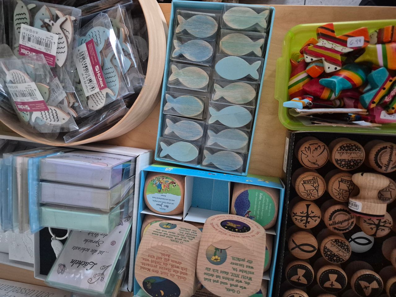 Ein Holztisch zeigt verschiedene Artikel, darunter fischförmige Stempel, verschiedene Stempel in Holzboxen und dekorative Gegenstände in Plastikbehältern. Es gibt auch Holzstempel und dekorative Fische.