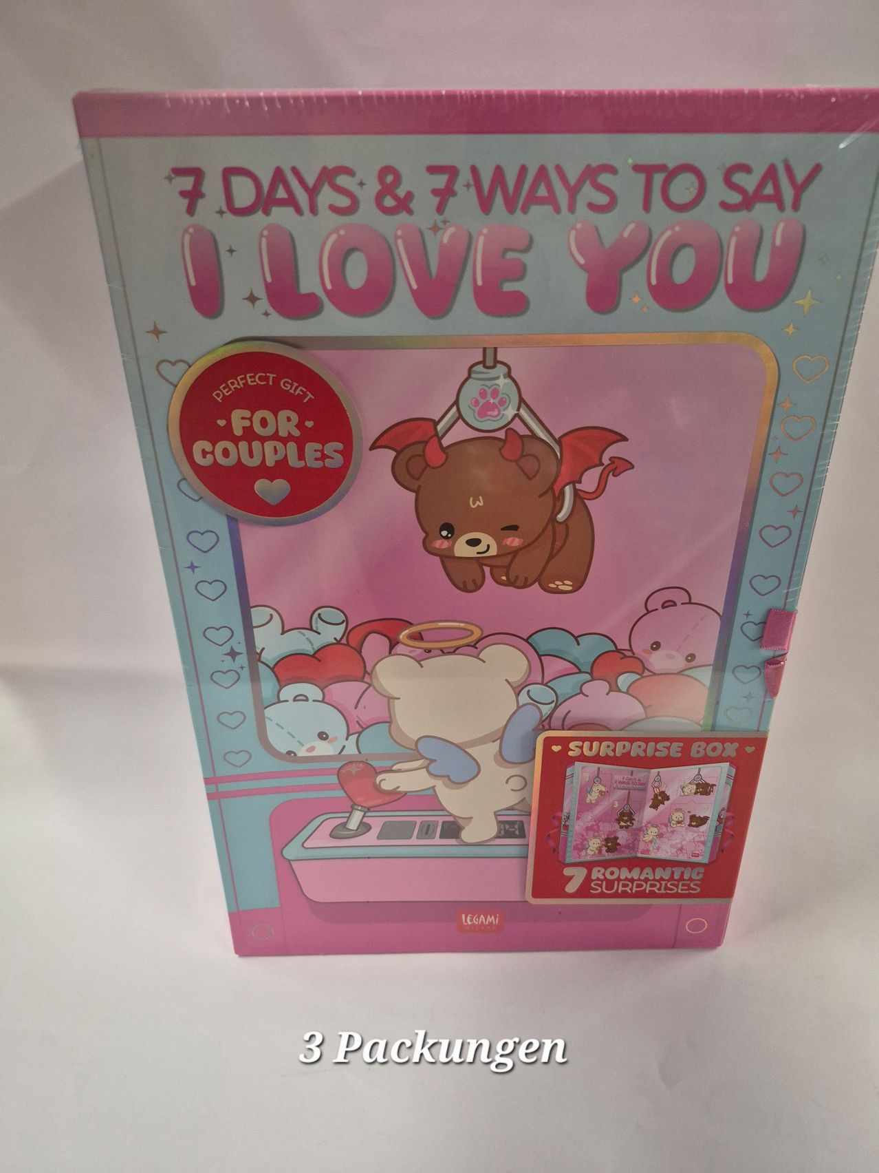 Eine pinke und blaue Box mit '7 Tage & 7 Wege, um I love you zu sagen' darauf. Es zeigt eine Cartoon-Illustration eines Bären mit Flügeln und einem Heiligenschein, der ein Herz hält und von anderen niedlichen Tieren umgeben ist. Die Box enthält eine Überraschungsbox mit 7 romantischen Überraschungen.