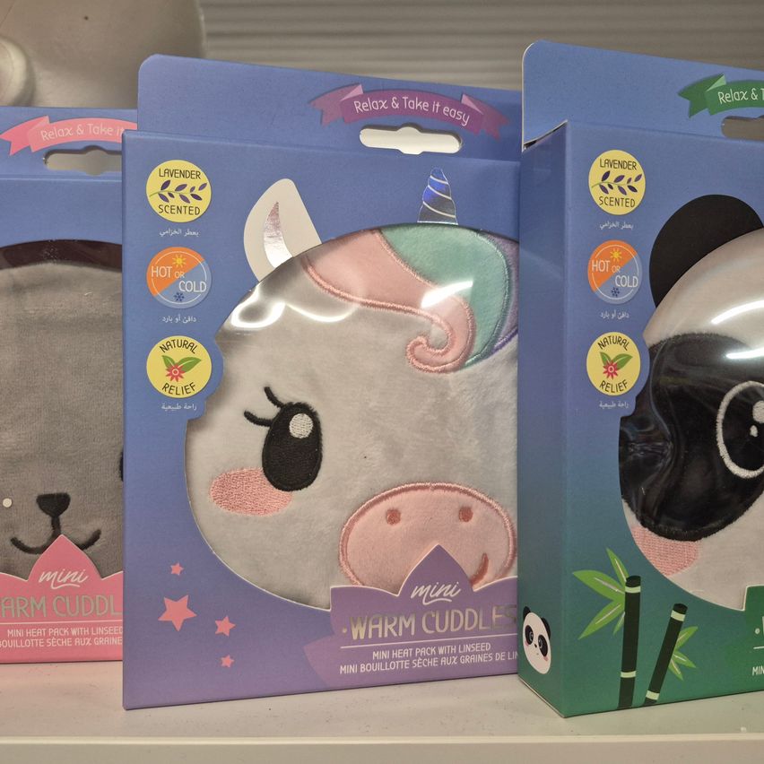 Drei lavendel-duftende Wärme-Kuscheltiere sind auf einem Regal ausgestellt. Links zeigt eines ein Einhorn, mittig ein Schwein und rechts ein Panda. Jedes hat ein kleines Etikett, das auf heiße oder kalte Anwendung hinweist.