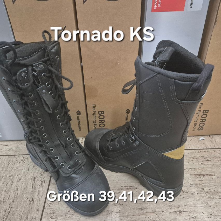 Ein Paar schwarze Tornado KS Stiefel mit gelben Akzenten wird auf einem Holzboden präsentiert, wobei die Größen 39, 41, 42 und 43 angegeben sind. Die Stiefel stehen vor braunen Kartons mit 'BORO' und 'Feuerwehrstiefel' Etiketten.