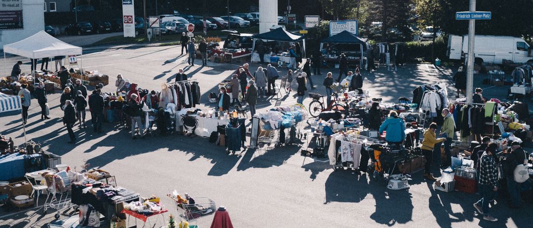 Ein Luftbild eines Flohmarkts mit vielen aufgestellten Ständen auf einer gepflasterten Straße mit mehreren umhergehenden Personen.