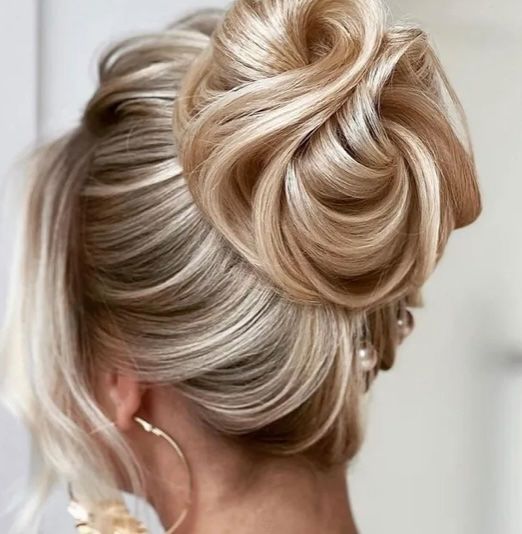 Eine Frau mit blondem Haar in einem Dutt mit losen Strähnen, die ihr Gesicht umrahmen, trägt Perlenohrringe und Creolen.