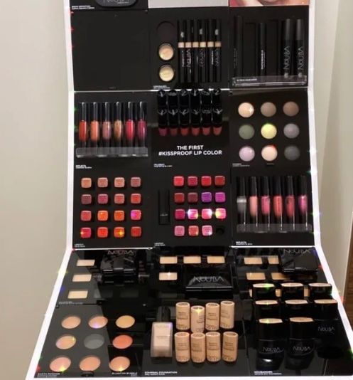 Eine Kosmetikanzeige präsentiert verschiedene Make-up-Produkte wie Lippenstifte, Lidschatten und Foundation in verschiedenen Farben. Der Markenname 'NOUVA' ist prominent sichtbar.