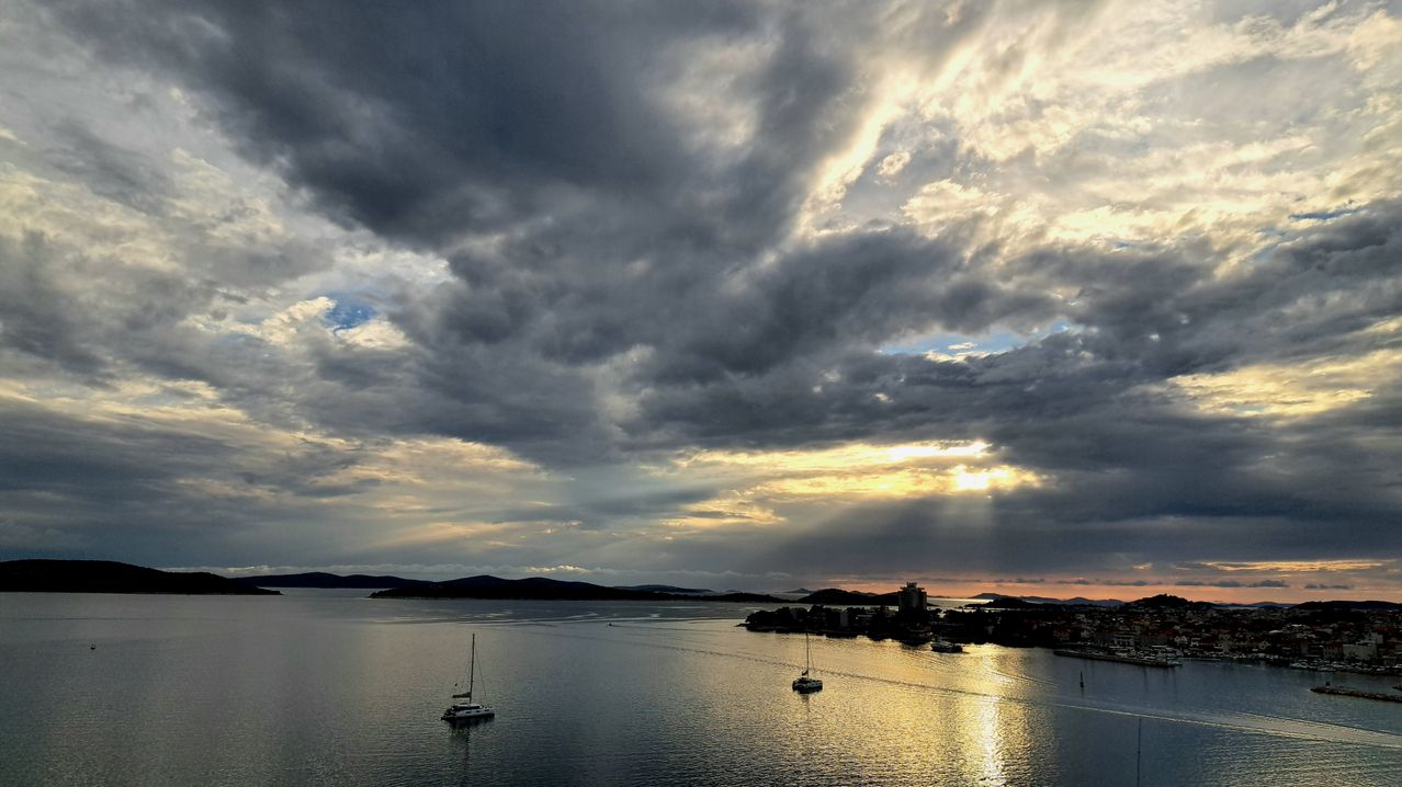 An aerial view of a body of water with two sailboats under a cloudy sky.