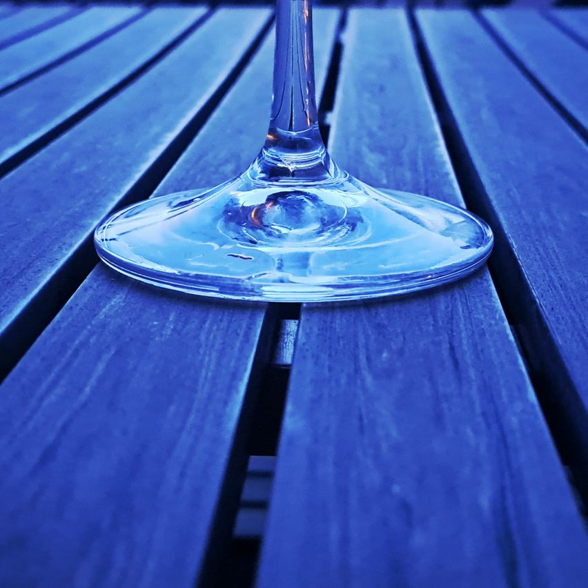 Ein klares Weinglas steht auf einem blauen Holztisch und reflektiert Licht von oben.