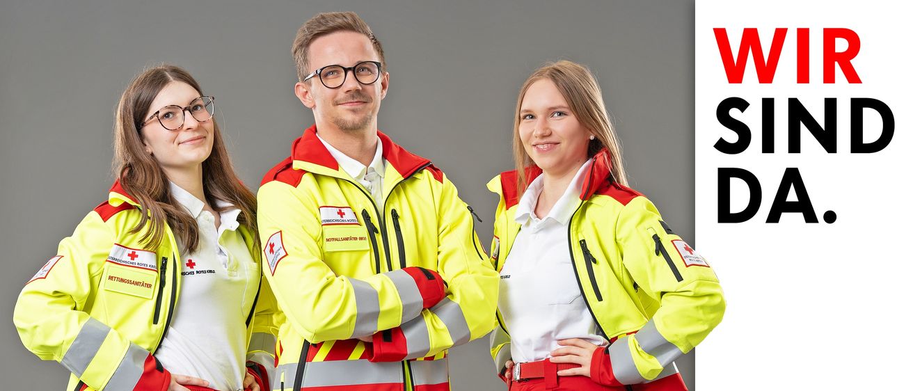 Zwei Personen in gelben und roten Notfalluniformen, lächelnd, und posieren für ein Foto.