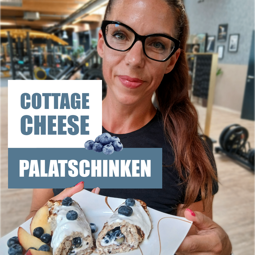 A woman in a gym holds a plate with cottage cheese and blueberries labeled 'Cottage Cheese Palatschinken'. She wears glasses and a black shirt.