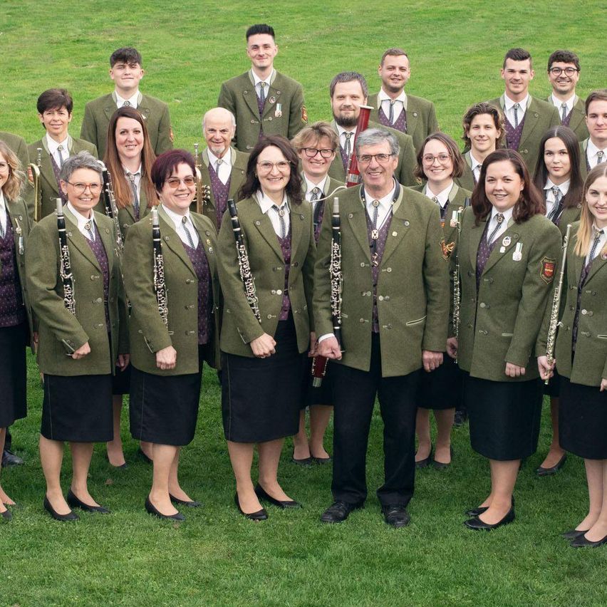 Eine Gruppe von Menschen in Uniformen und mit Musikinstrumenten posiert für ein Foto auf einem Rasenfeld.