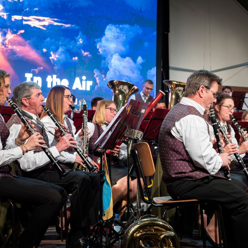 A group of musicians are performing on stage with various instruments. A projection of the sky is on the screen behind them.