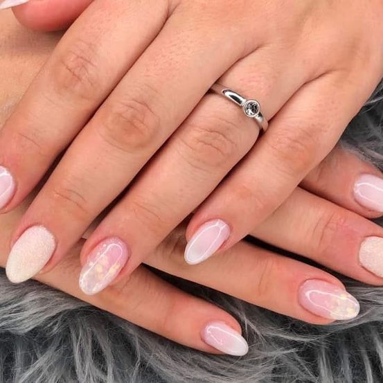 Hände mit gepflegten Nägeln, die einen silbernen Ring mit einem Edelstein auf einem grauen Pelzuntergrund zeigen.