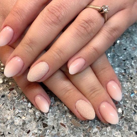 Ein Nahaufnahme von gepflegten Nägeln einer Person mit hellen rosa und beigen Farbtönen auf einer glitzernden Oberfläche.