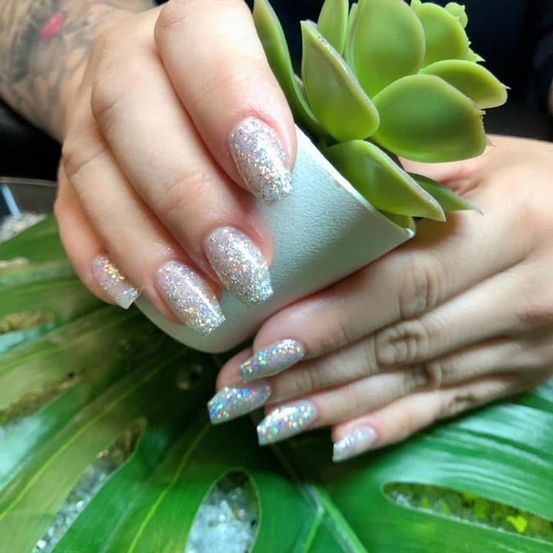 Eine Hand mit glitzernden Fingernägeln hält ein kleines Topfsukkulent auf einem grünen Blatt.