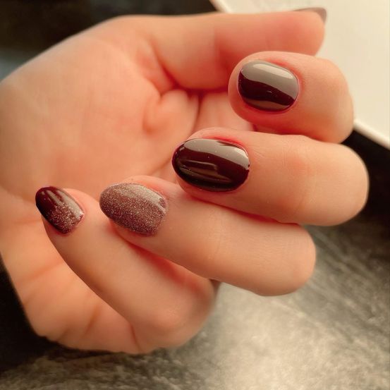 Ein Nahaufnahme einer Hand mit fünf dunkelburgunderfarbenen Nägeln. Der Daumen und der Zeigefinger haben eine punktierte Textur.