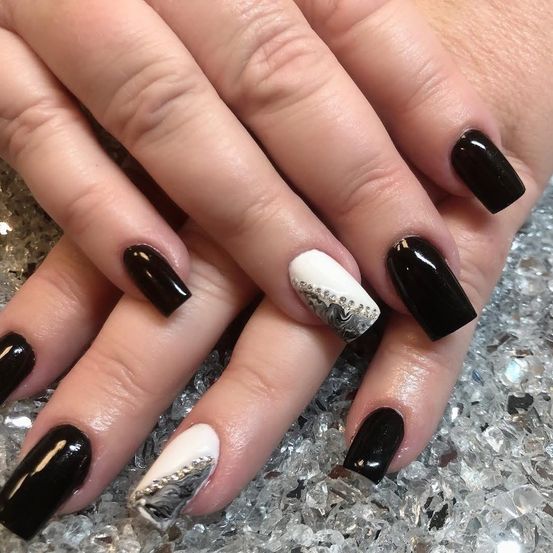 Nahaufnahme einer Hand mit schwarzem und weißem Nagellack, mit aufwendigen silbernen Designs auf den Nägeln. Die Nägel liegen auf einer glitzernden Oberfläche.