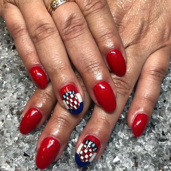 Eine Hand mit roten Nägeln, die einen roten, weißen und blauen karierten Design auf dem Daumen und Mittelfinger aufweisen.