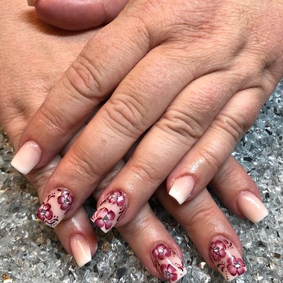 Ein Nahaufnahme einer Hand mit gepflegten Nägeln, die Blumendesigns auf einer cremefarbenen Basis aufweisen. Die Nägel sind leicht glänzend, und die Hand ruht auf einer glänzenden, reflektierenden Oberfläche.