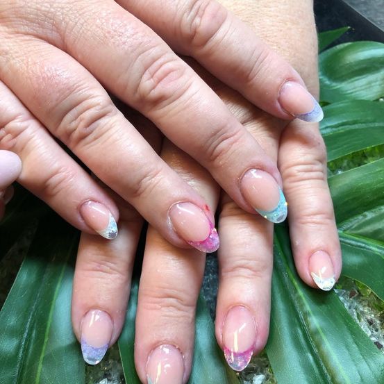 Ein Nahaufnahme von Händen mit gepflegten Nägeln. Jeder Nagel hat ein einzigartiges Design mit Rosa-, Blau- und Weißtönen.