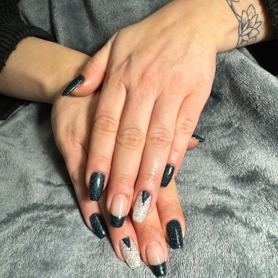 Zwei Hände mit schwarzen und silbernen Glitzernagellack liegen auf einer grauen Decke. Die Nägel haben verschiedene Designs.
