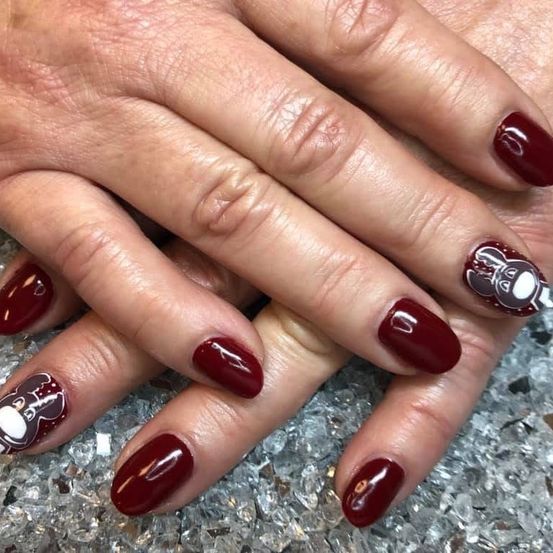 Ein Nahaufnahme von Händen einer Person mit rotem Nagellack. Jeder Nagel hat ein einzigartiges Design mit einem Bären, und die Nägel sind vor einem funkelnden Hintergrund angebracht.