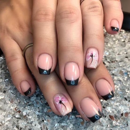 Ein Nahaufnahme einer Hand mit pinken und schwarzen Nageldesigns, die Blumenmotive auf einer glitzernden Oberfläche zeigen.