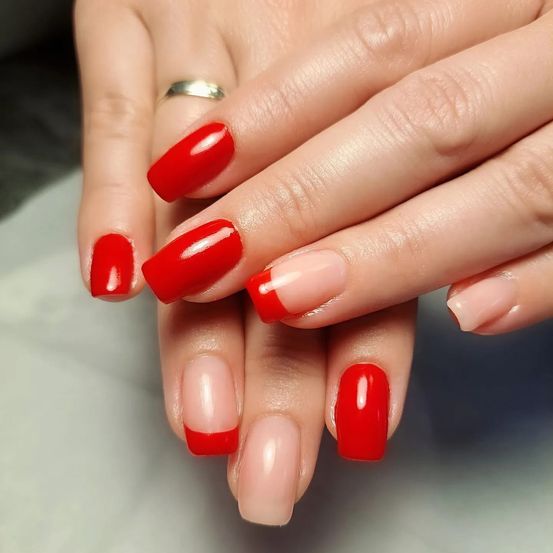 Ein Nahaufnahme der Hände einer Frau mit rotem und pinkem Nagellack. Ihre Nägel haben einen glänzenden Finish.