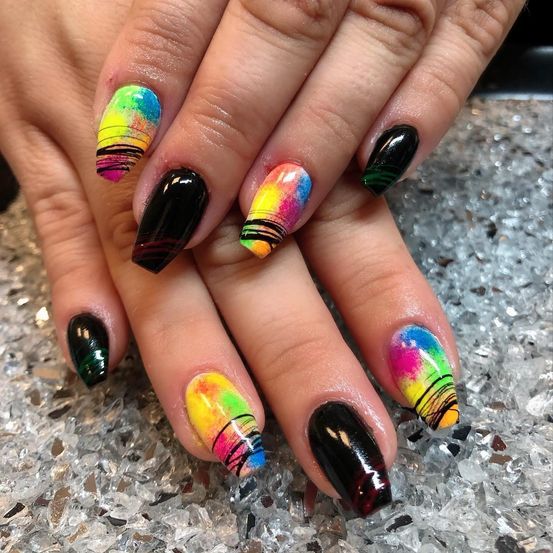 Ein Nahaufnahme einer Hand, die Nägel mit leuchtenden, mehrfarbigen Designs zeigt, einschließlich Gelb, Orange, Pink und Grün, mit schwarzen Basen und stiftartigen Mustern.