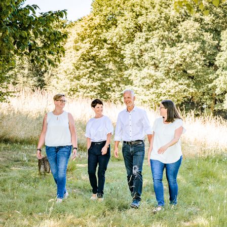 Fünf Menschen, wahrscheinlich eine Familie, gehen gemeinsam auf einem Grasfeld. Sie sind lässig gekleidet.