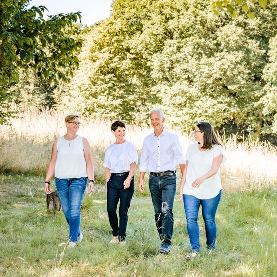 Fünf Menschen, wahrscheinlich eine Familie, gehen gemeinsam auf einem Grasfeld. Sie sind lässig gekleidet.