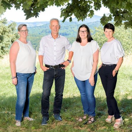 Vier Personen, zwei Frauen und zwei Männer, stehen zusammen in einem Feld mit Bergen im Hintergrund. Sie alle lächeln.