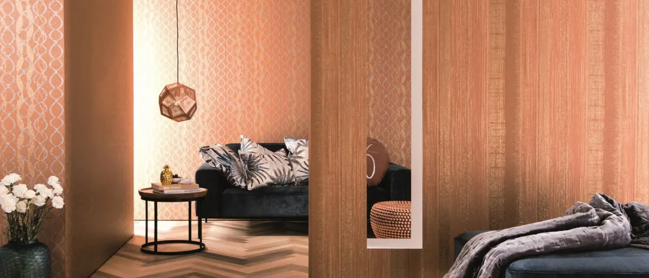 Ein modernes Wohnzimmer mit einem blauen Sofa, gemusterten Tapeten und einer dekorativen Lampe, die an der Decke hängt. Ein Tisch mit Büchern und einem goldenen Objekt befindet sich in der Nähe.