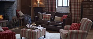 Ein Wohnzimmer mit einem braunen Ledersofa, einem gestreiften Ottoman und einem weißen Pelzteppich auf dem Boden. Eine Lampe steht auf einem Tisch neben dem Sofa.