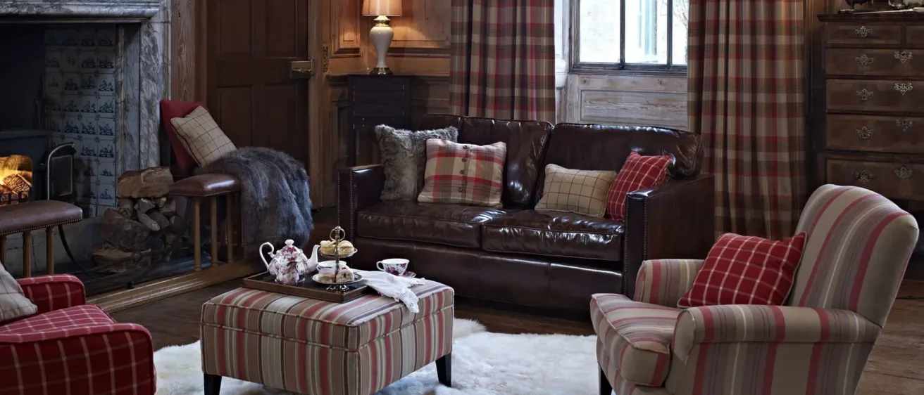 Ein Wohnzimmer mit einem braunen Ledersofa, einem gestreiften Ottoman und einem weißen Pelzteppich auf dem Boden. Eine Lampe steht auf einem Tisch neben dem Sofa.