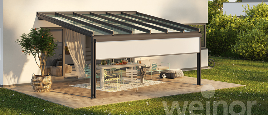 Ein modernes Haus mit einer Glasdach-Terrasse und einer Terrasse mit Tisch, Stühlen und einem Topf. Das Haus hat mehrere Fenster und eine weiße Wand.