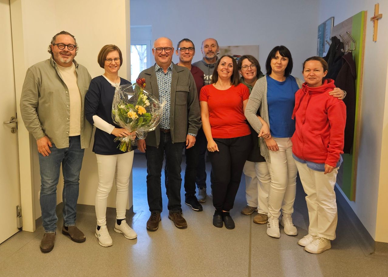 Eine Gruppe von Menschen posiert für ein Foto in einem Raum, wobei eine Person einen Blumenstrauß hält.